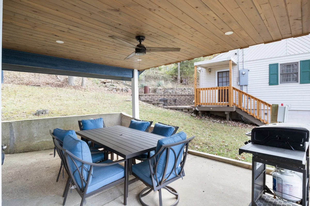A covered outdoor dining area featuring a wooden ceiling, a dining table with blue chairs, and a grill. The space feels sheltered yet open, inviting guests to enjoy family-style meals in an elegant, airy setting connected to the outdoors.
