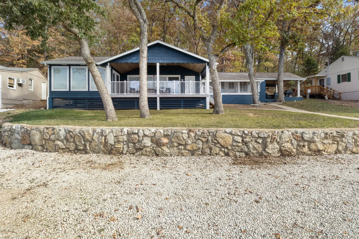 This image showcases the blue facade of the house with a spacious porch, surrounded by trees and a stone wall. The inviting exterior suggests both privacy and a welcoming atmosphere. The porch is ideal for family gatherings or simply relaxing while enjoying the natural beauty of the surroundings.