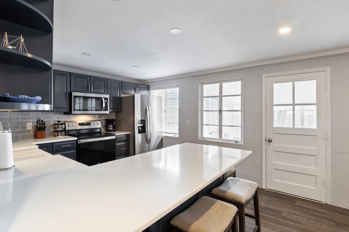 A modern kitchen with a spacious island, stainless steel appliances, open shelving, and a window that lets in plenty of light. The setup is inviting for both cooking and socializing, with bar stools to encourage casual conversation.