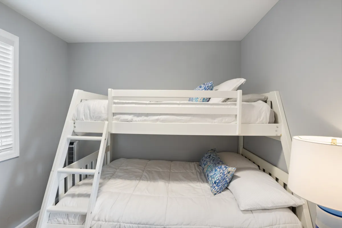 A playful bedroom nook featuring a bunk bed dressed with decorative pillows and a lamp for cozy nighttime reading. The arrangement suggests a welcoming, comfortable spot ideal for kids or friends sharing a room.