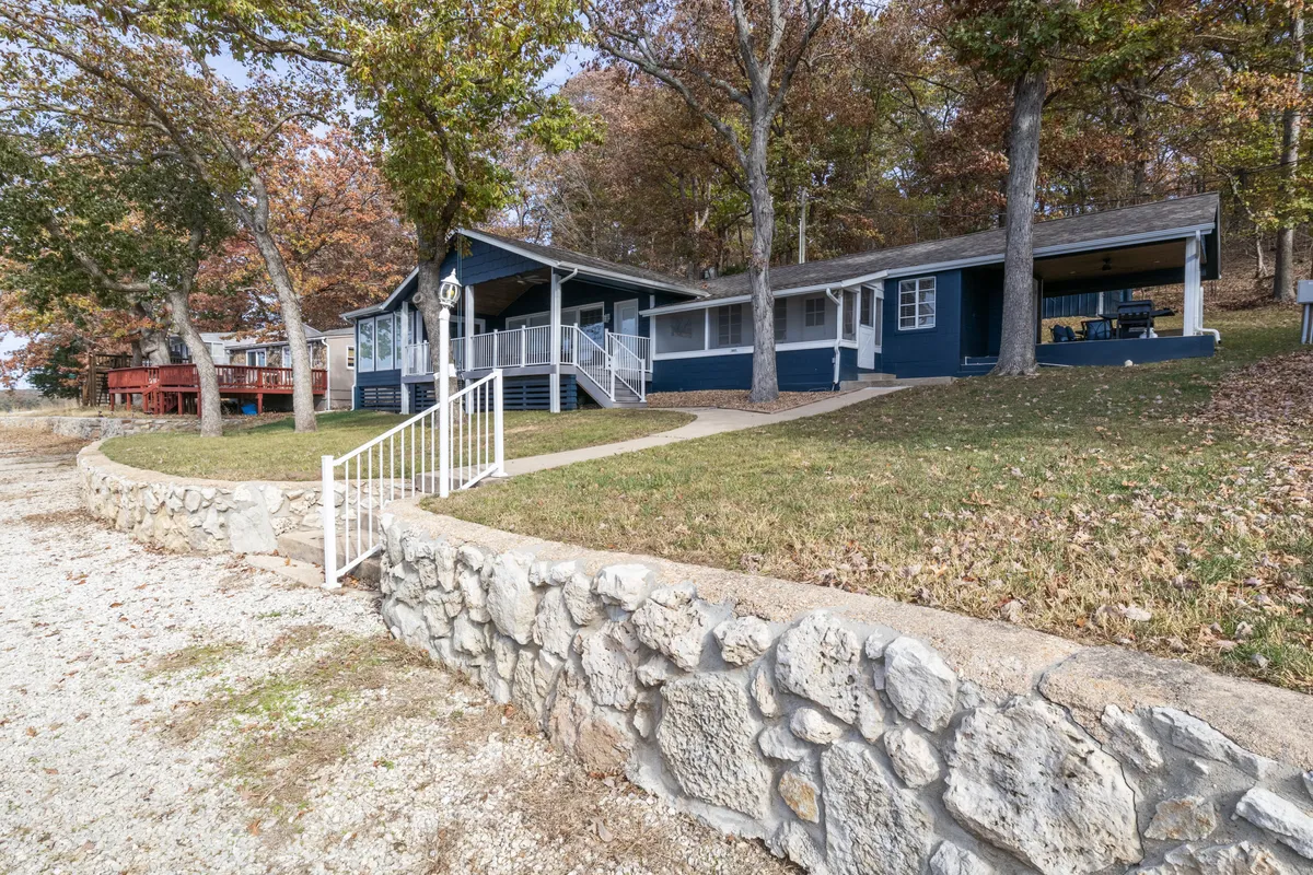 This exterior view captures the blue house with a stone wall, green lawn, and trees adorned with autumn leaves. There's plenty of room for outdoor activities, and the house appears welcoming for families and their pets alike.