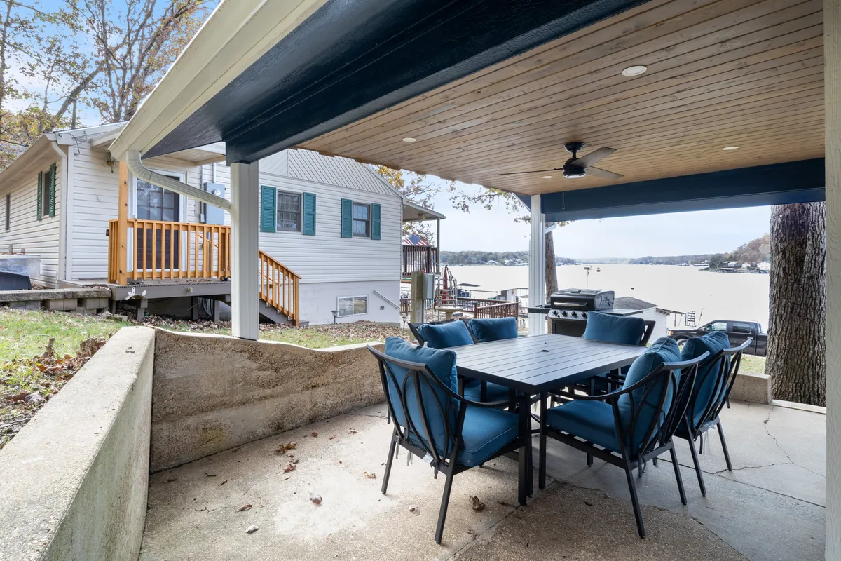 A spacious outdoor dining table is set under the open sky, facing a picturesque view of the lake and neighboring homes. The setting suggests family meals, celebrations, and morning coffee enjoyed in the great outdoors, with water always in view.