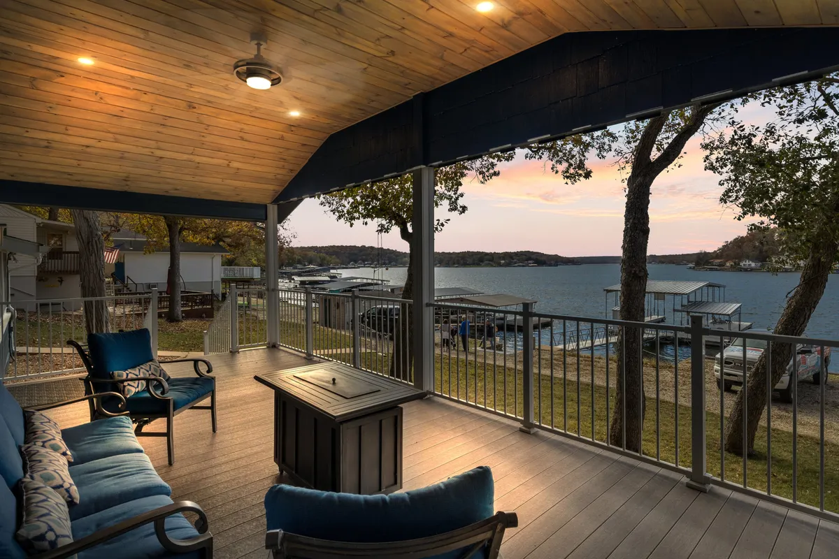 The image showcases a serene outdoor seating area overlooking a tranquil lake, with a cozy fire pit table at the center. Comfortable chairs invite guests to relax and unwind, while the backdrop features calm, sparkling waters and the promise of stunning sunset views. The scene is perfect for gathering, enjoying a barbecue, or savoring a quiet morning coffee as the sun rises or sets over the water.